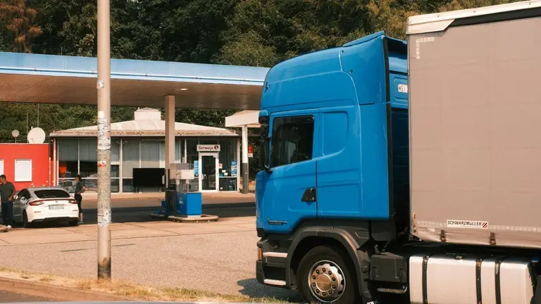 Caminhão azul com carreta parado ao lado de um posto de combustível