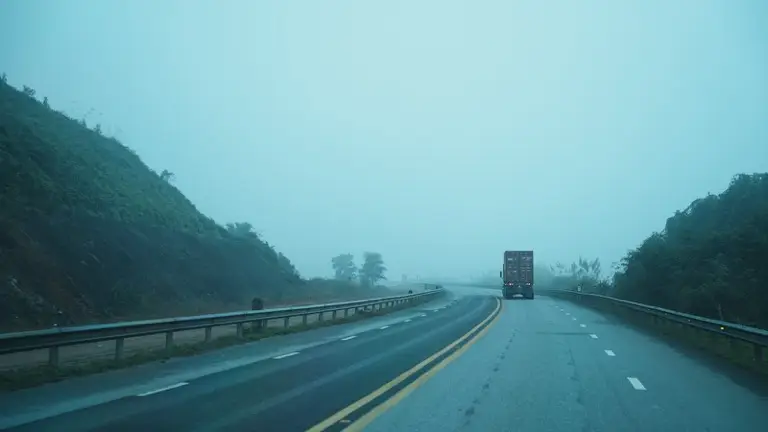 Carreta subindo uma serra em rodovia com neblina, vista pela traseira