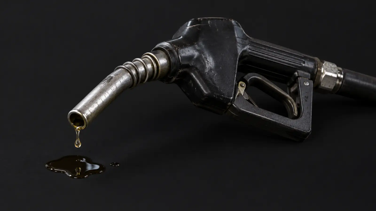 Bico de bomba de combustível gasto, pingando diesel numa pequena poça sobre fundo preto