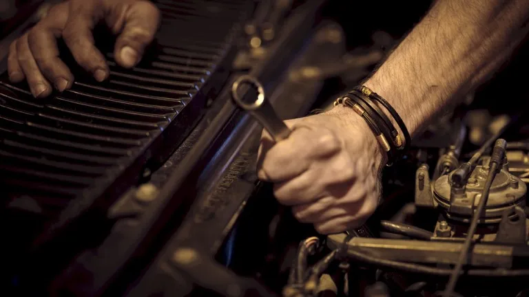 Mãos de mecânico apertando uma peça do motor com chave fixa